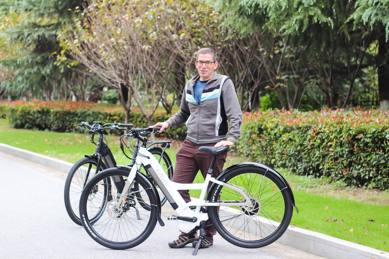 Man with two electric bicycles enjoying a day outdoors in a park setting.